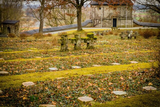 Alee umbrită într-un cimitir vechi, cu cruci de piatră acoperite de mușchi și copaci bătrâni
